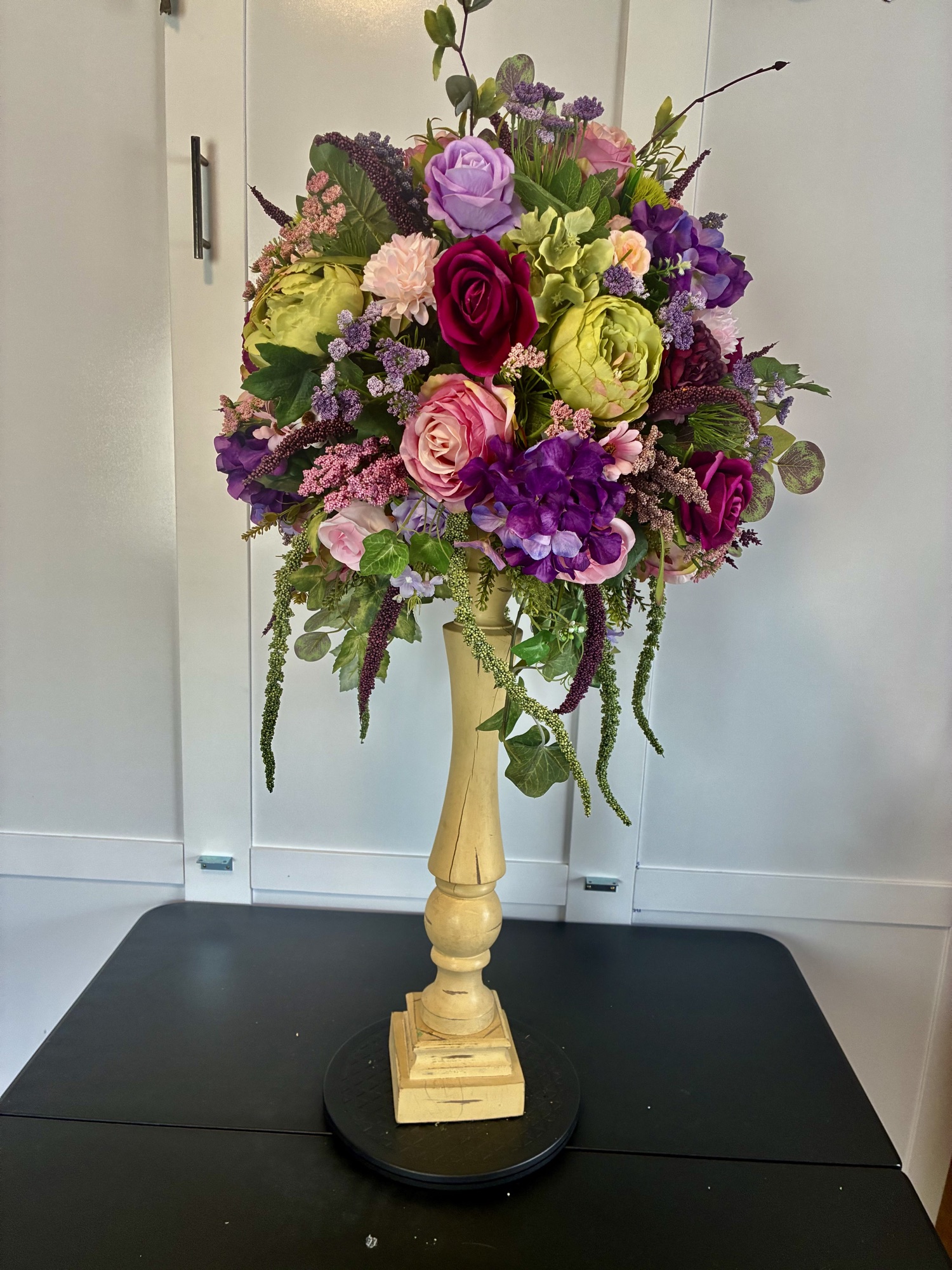 A lavish arrangement of lavender roses, ranunculus and garden greenery on a wooden pedestal